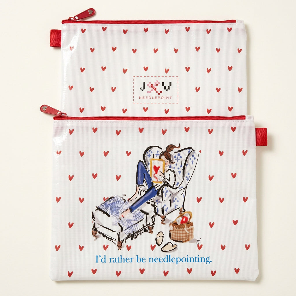 Two white zippered pouches with a repeating red heart pattern, shown on a white surface. The top pouch has a small embroidered cross-stitch style 'JOY' patch, and the bottom pouch features a needlepoint illustration of a woman in an armchair with the text 'I'd rather be needlepointing.