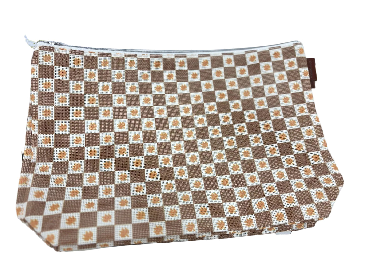 A fabric zippered pouch with a brown and cream checkerboard pattern featuring small orange maple leaf motifs in the center of each square, displayed on a white table surrounded by sewing supplies.