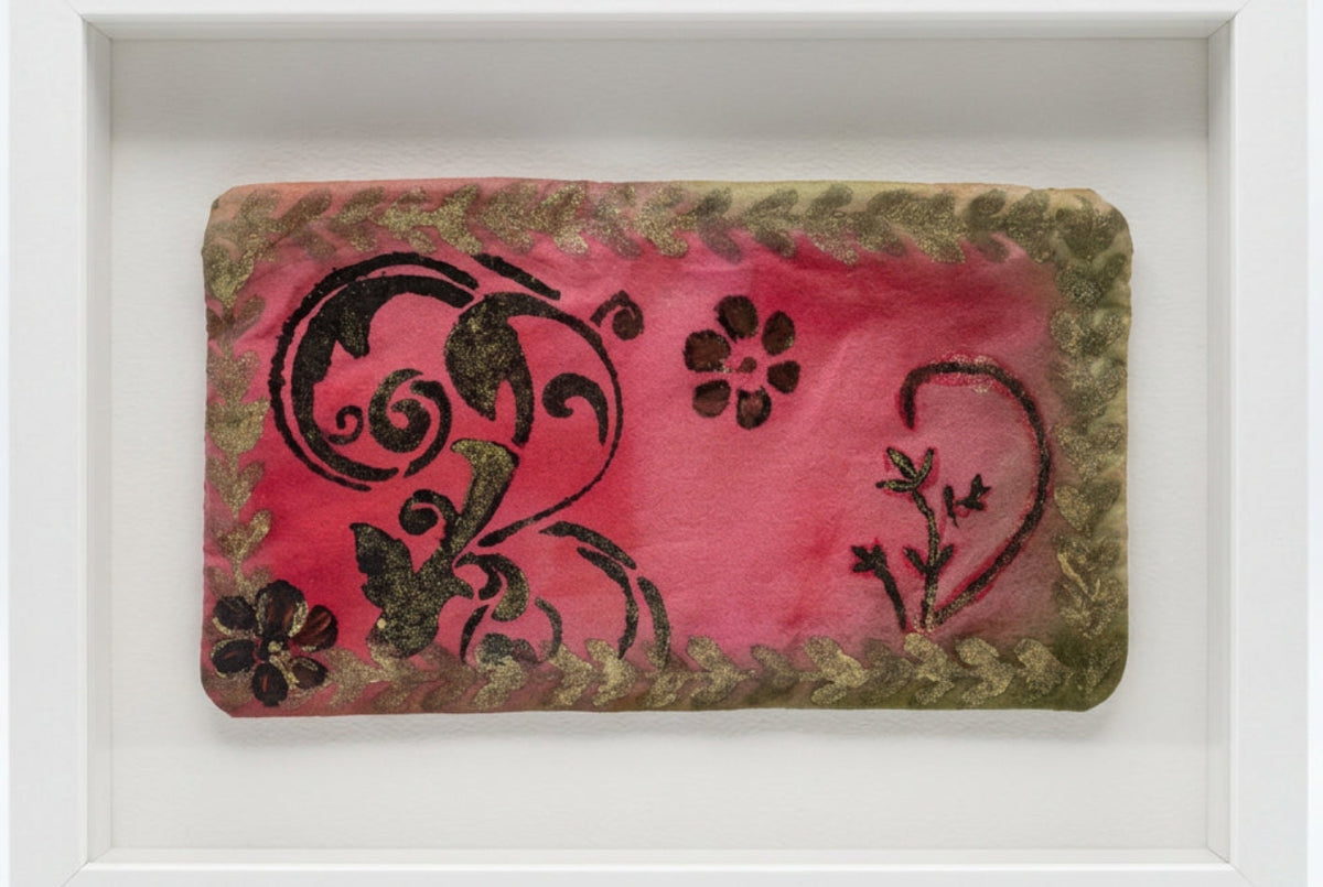 A rectangular fabric pouch or clutch with a pink center, black floral and scroll motifs, and a distressed olive-brown border, photographed on a white surface.