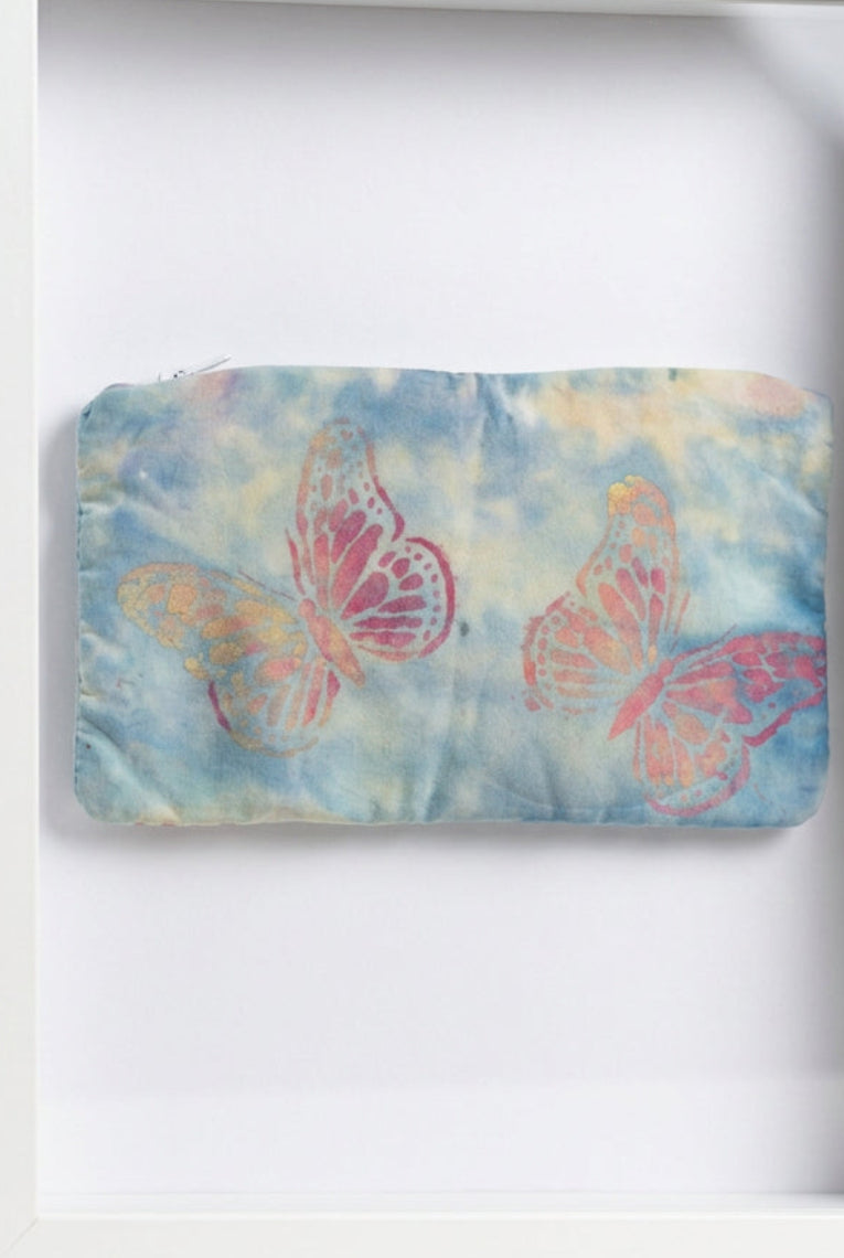A rectangular fabric pouch or clutch with a light blue and gray tie-dye pattern, featuring two pink and orange butterfly designs.