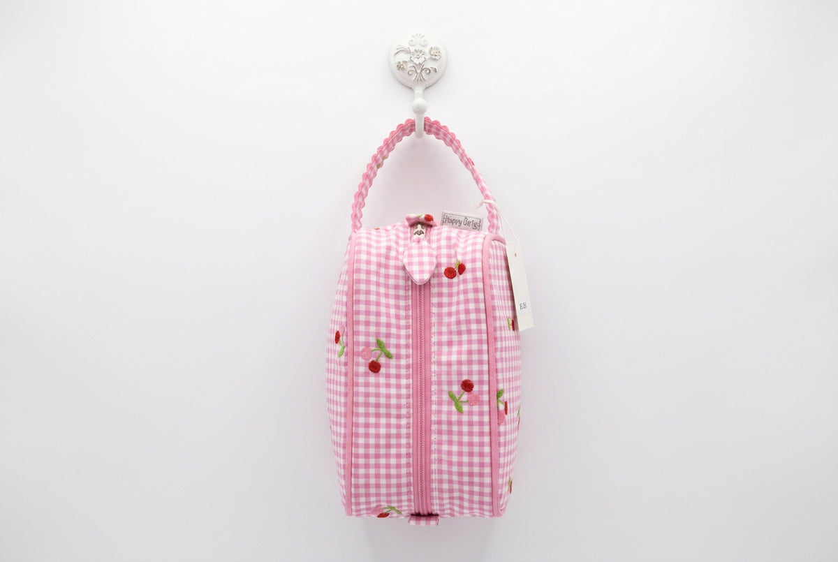 A pink and white gingham zippered pouch with cherry embroidery, featuring a matching pink scalloped strap and a 'Hobby Gift' tag, shown on a white table with a busy background.