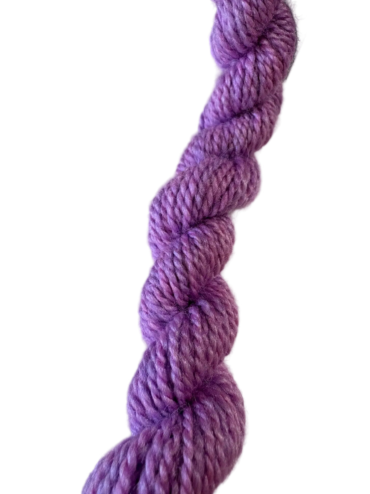 A close-up of a twisted skein of variegated purple yarn, showing shades of lavender and violet, with a green and black product tag partially visible at the top.