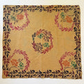 A square beige fabric panel with a hand-painted floral and leaf pattern, laid flat on a dark work surface. The design features pink, orange, green, and brown motifs on a warm beige background, with a matching patterned border.